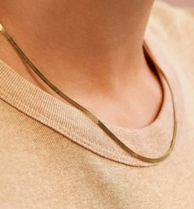 Dettaglio della collana a catena piatta a serpente dorata su collo di una modella