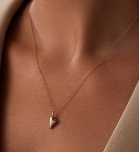Close-up of a polished golden heart pendant with a fine minimalist chain on a model