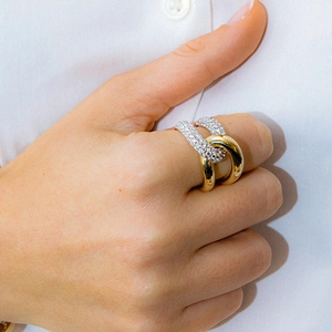 Interlocking silver pavé and gold band ring shown on a finger with white shirt background