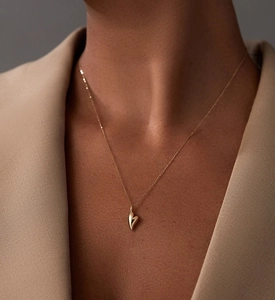 Detail of a shiny gold 3D heart pendant necklace worn on a beige suit jacket