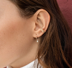 Close-up of a gold ear cuff and earring with a round sparkling zircon pendant on model