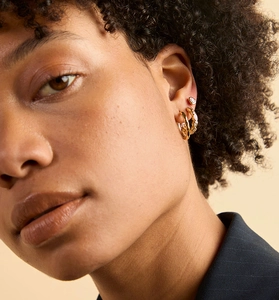 Close-up of gold twisted hoop earrings and pear-cut crystal stud on female ear