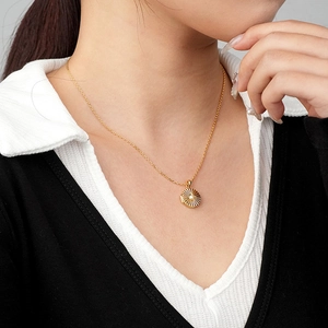 Gold starburst medallion necklace with a central pearl on a simple link chain worn by a model