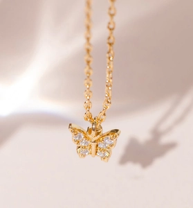 Macro detail of gold butterfly necklace with pavé crystal wings and artistic shadow