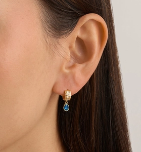 Close-up of golden teardrop hoop earrings with blue zircon stones on model's ear