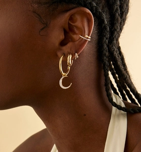 Detail of gold star and moon earrings with micro-inlaid stones on a female model