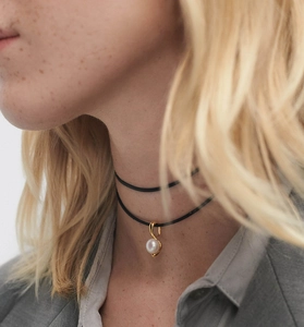 Gros plan d'un collier de perles avec pendentif en or en S sur cordon noir