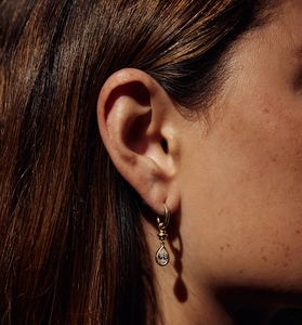 Macro detail of teardrop zircon earrings in gold plating worn by model during photoshoot