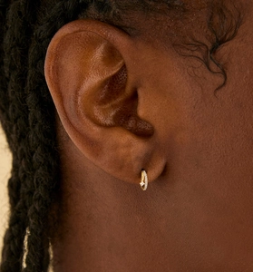 Detail of a small gold hoop earring featuring micro-pave white crystals on a model's ear