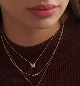 Détail d'un collier doré multicouche avec pendentif papillon pavé et pierres de zircon