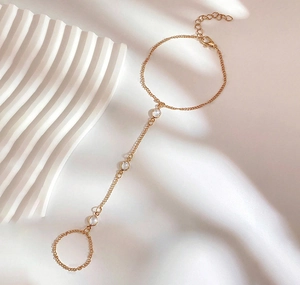 Dettaglio di un bracciale ad anello dorato con tre cristalli tondi su sfondo minimalista