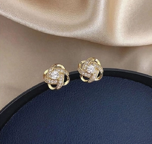 Macro shot of gold twist earrings with central zircon and pavé diamonds on blue velvet