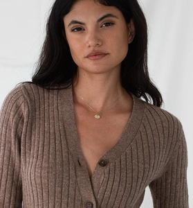 Detail of gold oval zodiac pendant necklace worn on a brown ribbed knit cardigan