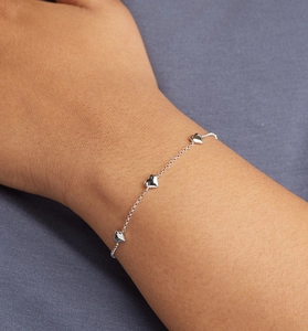 Gros plan de trois breloques cœurs en argent sur un bracelet chaîne porté au poignet