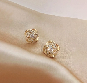 Detailed view of gold clover knot earrings with pavé zircons on champagne silk fabric