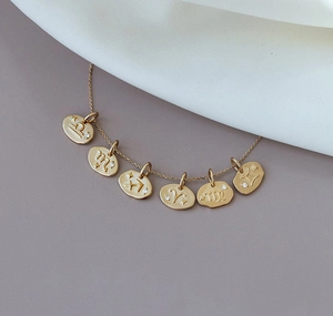 Macro detail of gold zodiac coin necklace with six engraved pendants and zircon accents