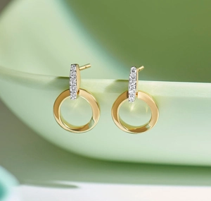 Close-up of gold geometric drop earrings with diamond pavé bar on a ceramic surface