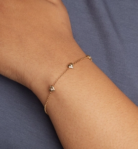 Gros plan d'un bracelet en or avec cœurs en zircone porté sur un fond en tissu bleu