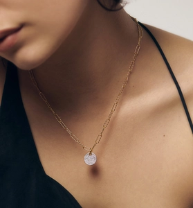 Gros plan d'un collier chaîne trombone dorée avec pendentif rond serti de zircons brillants