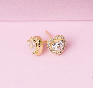 Detailed close-up of heart-shaped gold stud earrings with clear zircon stones on pink base
