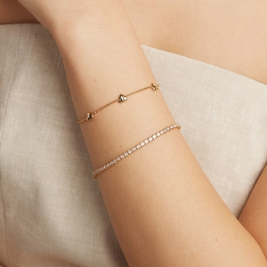 Bracelet à breloques cœur doré superposé avec bracelet tennis en argent sur le poignet