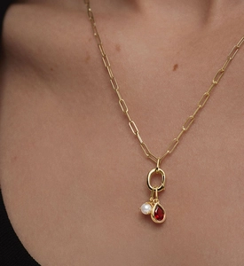 Detail of paperclip gold chain necklace with a white pearl and a red teardrop gemstone