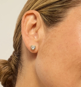 Close-up of a heart-shaped gold earring with a large zircon center on a female model