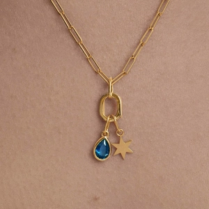 Gold paperclip necklace with blue teardrop gem and star charm on warm background