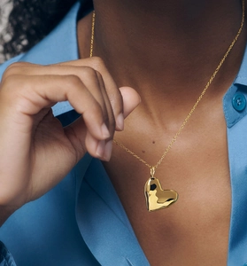 Macro detail of a polished gold heart-shaped locket necklace worn on a blue shirt