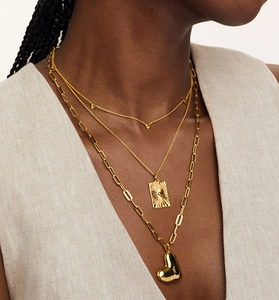 Close-up of three-layered gold heart necklace featuring paperclip chain and rectangular pendant