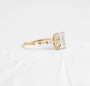 Detail of emerald cut zircon center stone with baguette side diamonds on gold ring