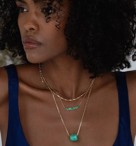 Detail of layered gold necklaces with emerald green stones and a turquoise pendant