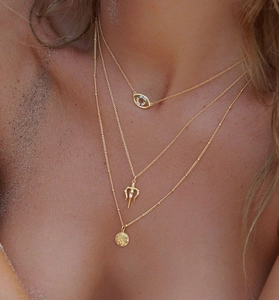 Detailed view of layered gold necklace set with evil eye and star coin on model skin