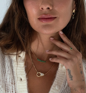 Detailed view of gold chain necklaces with green gemstones layered on a knit sweater