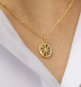 Macro detail of gold coin pendant with sunburst texture and sparkling zircon on Saturn chain