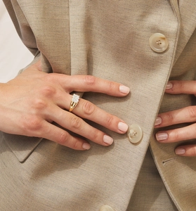 Close-up of elegant gold ring with pave-set cubic zirconia worn on a beige blazer