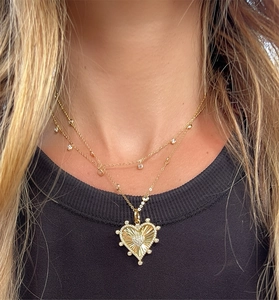 Detail of gold double-layered necklace featuring a sunburst heart pendant and zircon accents
