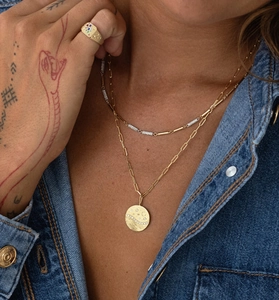 Detail of layered gold necklaces with moon star coin pendant and colorful gemstone ring