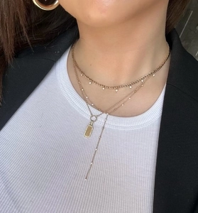 Detailed view of layered gold necklace with flat chain and rectangular pendant charms