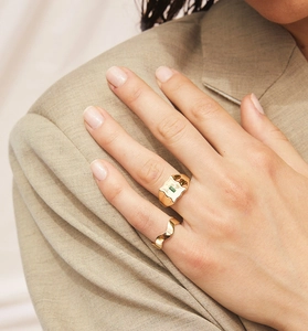 Detail of gold rings with green emerald stone on a model wearing an olive blazer