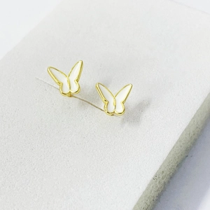 Close-up of gold butterfly stud earrings with white enamel wings on a grey display card