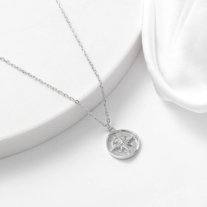 Close-up of S925 sterling silver compass coin pendant on white silk fabric background