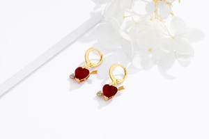 Détail de boucles d'oreilles cœur en argent 925 doré avec pierre rouge et flèche