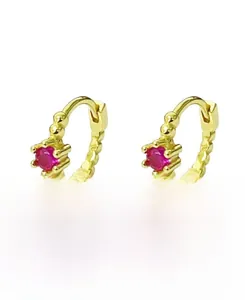 Détail macro de boucles d'oreilles huggie dorées avec zircon rouge et spirale perlée