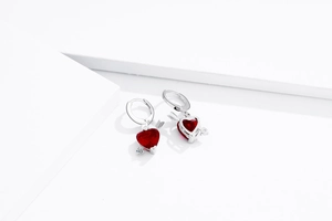 Détail macro de boucles d'oreilles cœur en argent avec zircon rouge et flèche