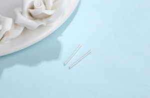 Détail macro de clous d'oreilles en argent fin 999 polis sur fond bleu minimaliste