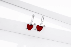 Détail de boucles d'oreilles flèche de Cupidon avec cœurs rouges sur socle blanc épuré
