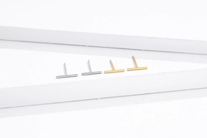 Close-up of minimalist S925 silver and gold bar stud earrings on white podiums