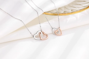 Detailed view of interlocking silver and rose gold heart necklaces on white satin fabric