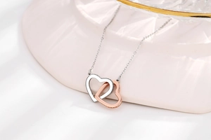 Macro view of interlocking silver and rose gold heart pendants with pavé set details